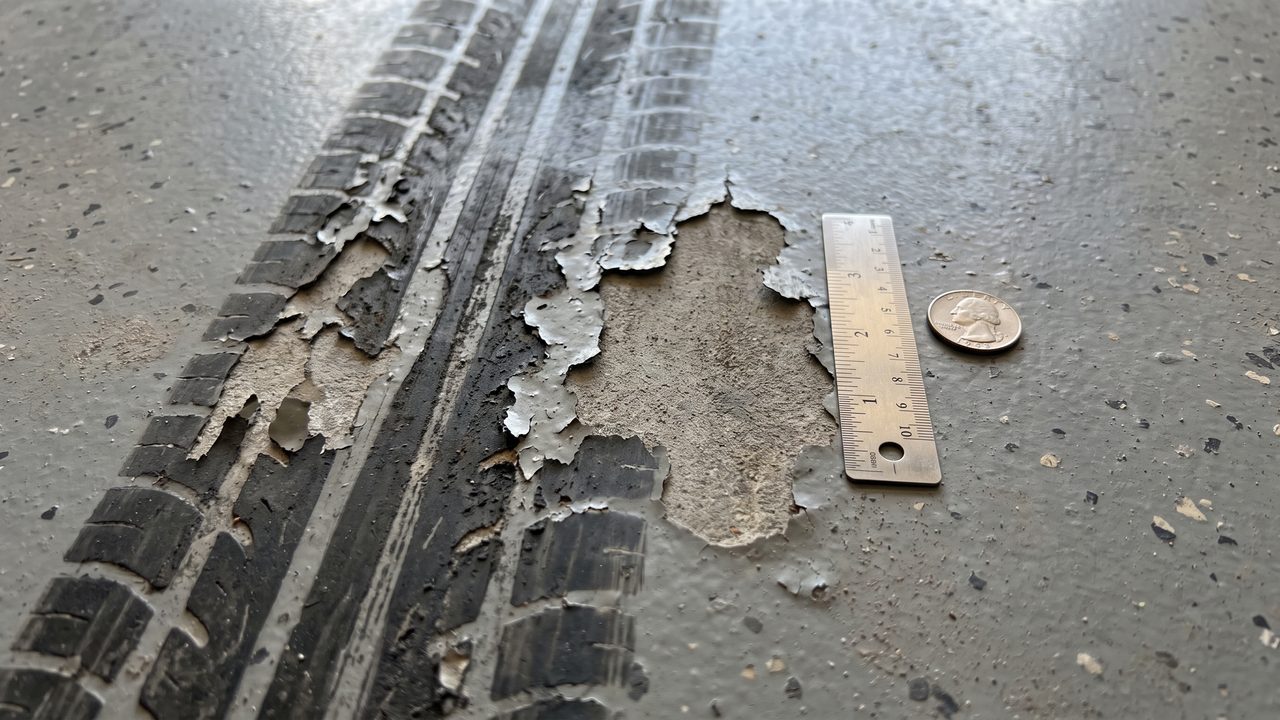 Epoxy garage floor Phoenix hot tire pickup and peeling damage close-up with ruler for scale